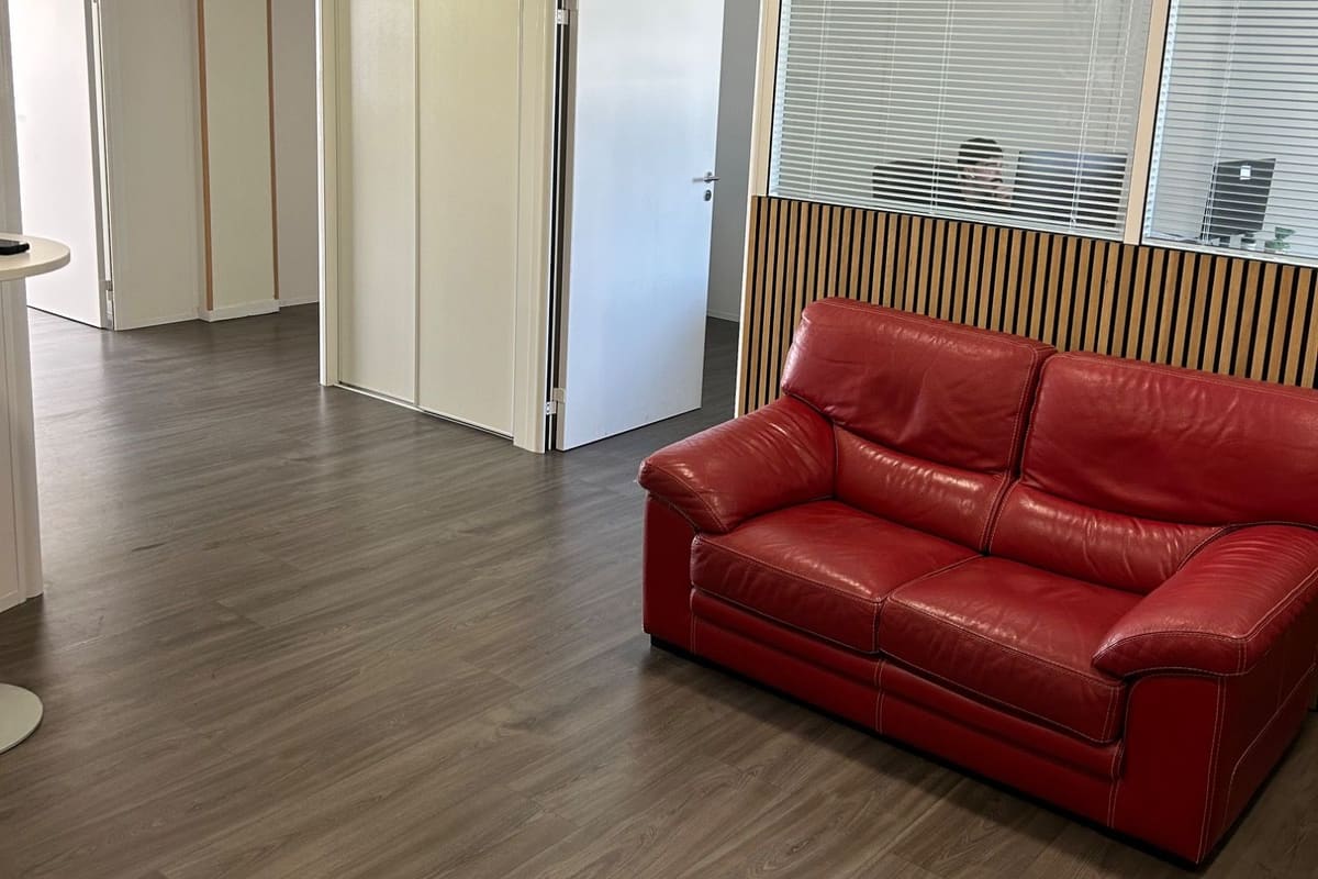 Plateau de bureaux entretenu par AGYL : cloisons vitrées, parquet propre et canapé rouge